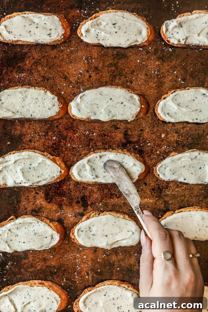 A hand using a knife to spread cheese on toasts.