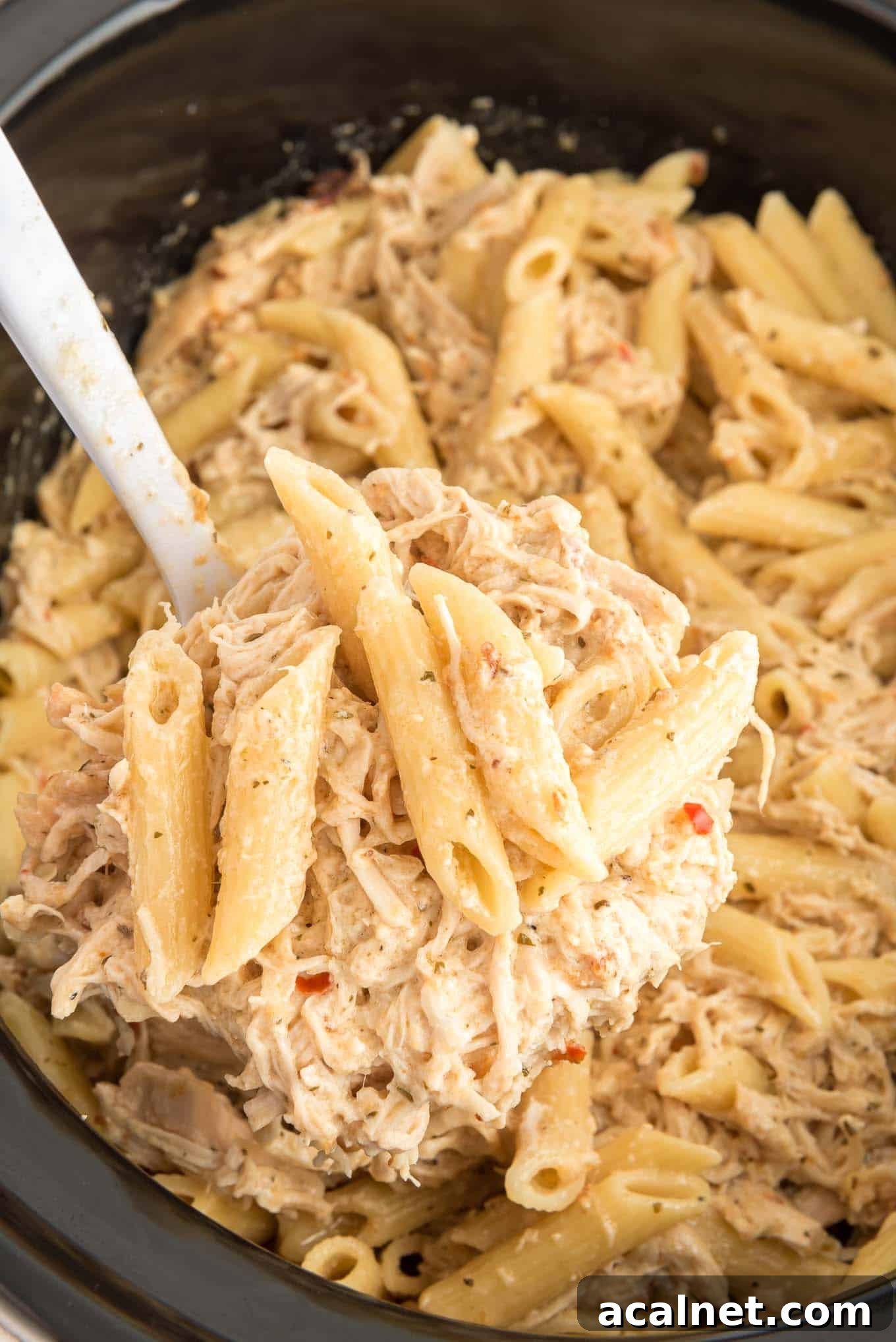 Garlic Parmesan Chicken Pasta with BWW Parmesan Garlic sauce in a crockpot with a serving spoon. 