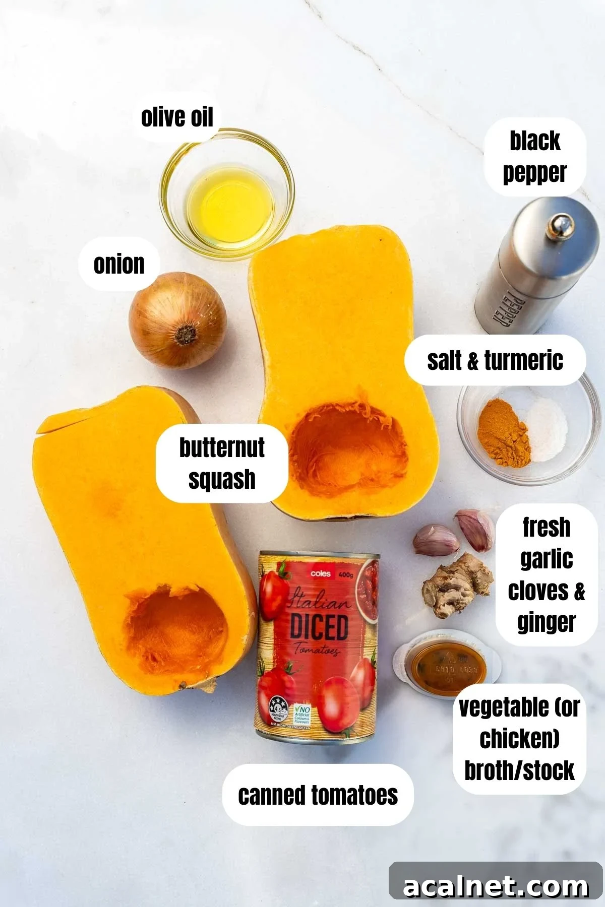 Creamy Roasted Butternut Squash and Tomato Soup Recipe 3 Overhead of all the ingredients needed to make a butternut squash and tomato soup, labelled, including 2 butternut squash halves, an onion, olive oil, canned tomatoes, vegetable broth, fresh garlic cloves and ginger, salt and turmeric, and black pepper.