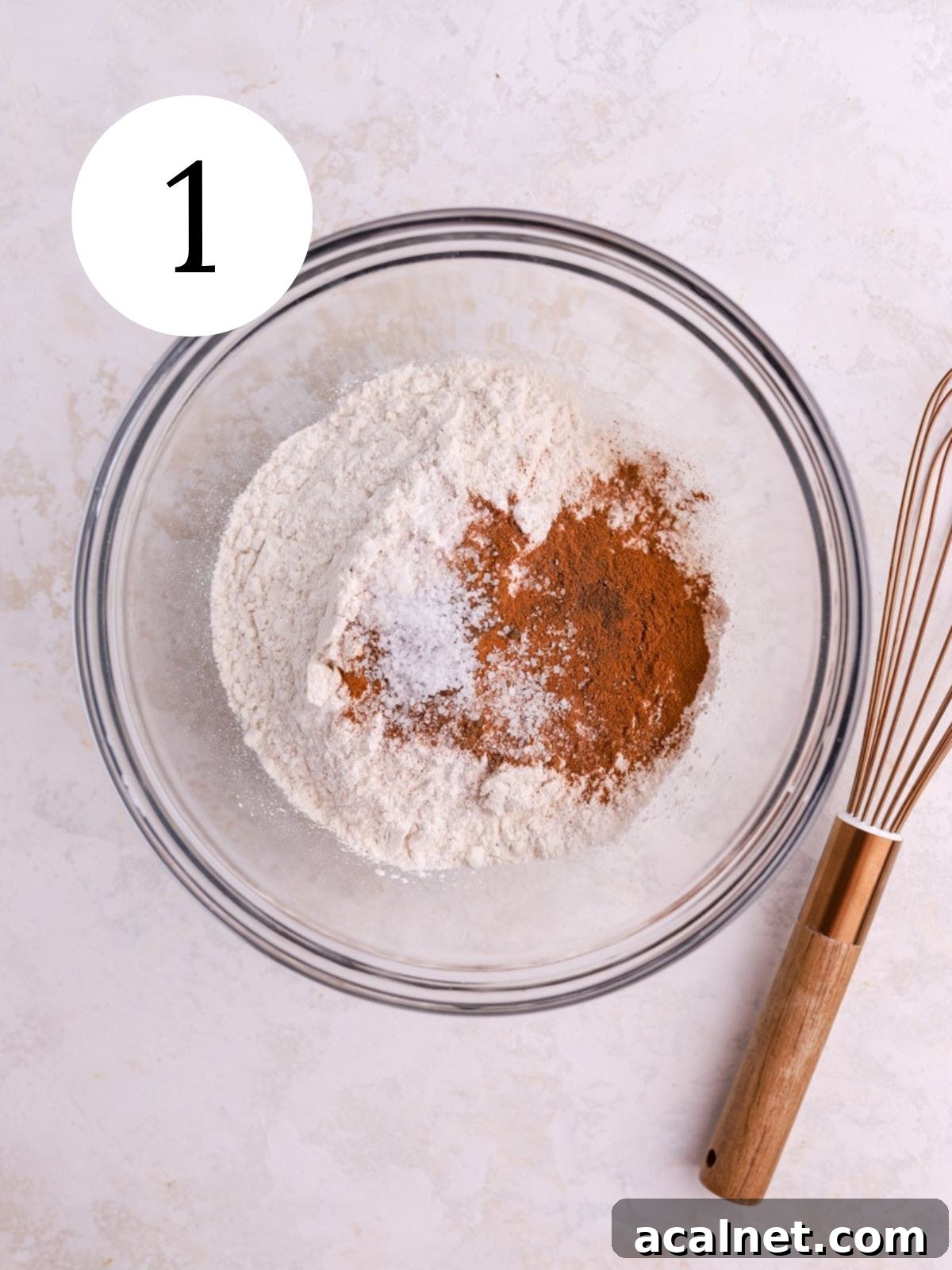 A mixing bowl with flour, spices, and salt and a whisk next to it. 