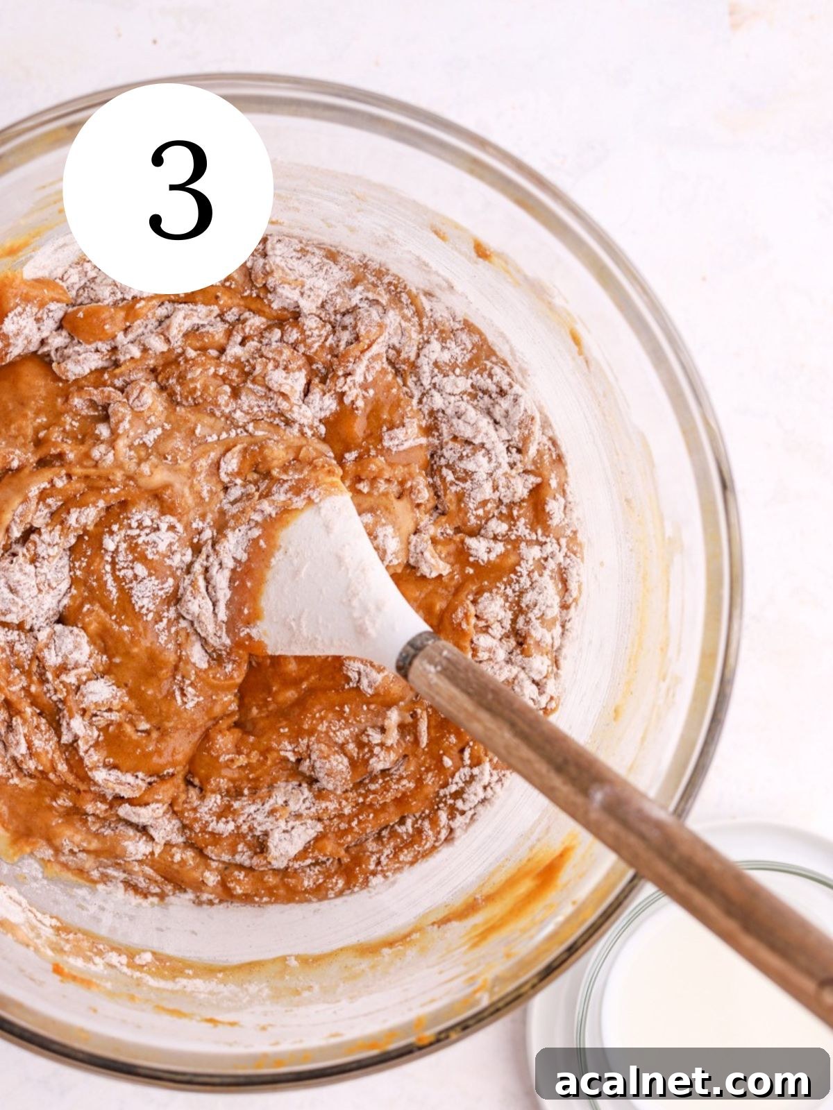 Flour being mixed into pumpkin cake batter with a spatula. 