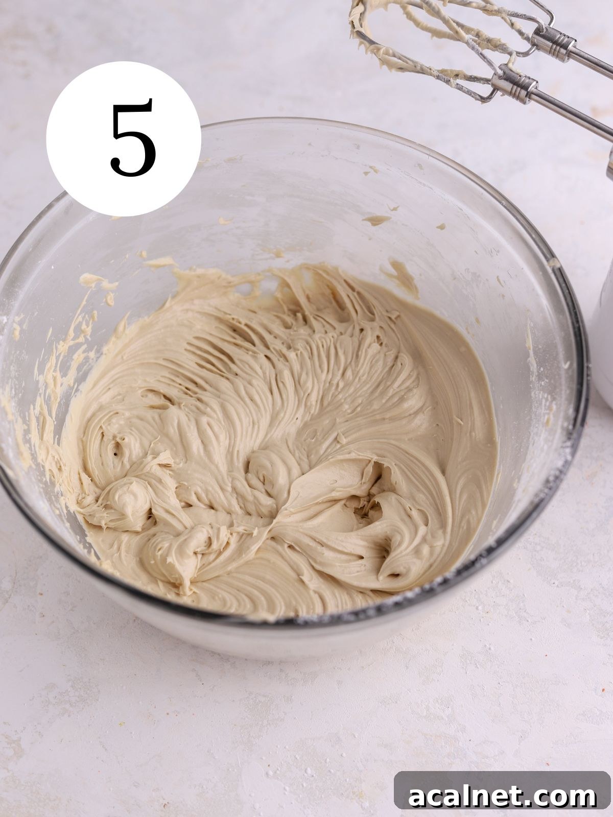 A glass mixing bowl with brown sugar cream cheese frosting mixed together. 