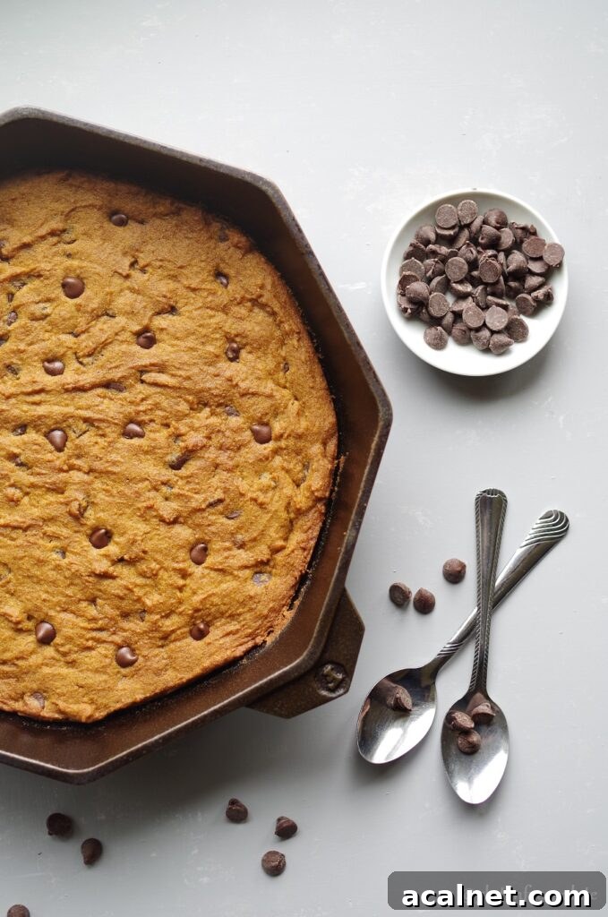 gluten free pumpkin chocolate chip skillet cookie in a cast iron skillet next to two spoons and a bowl of chocolate chips