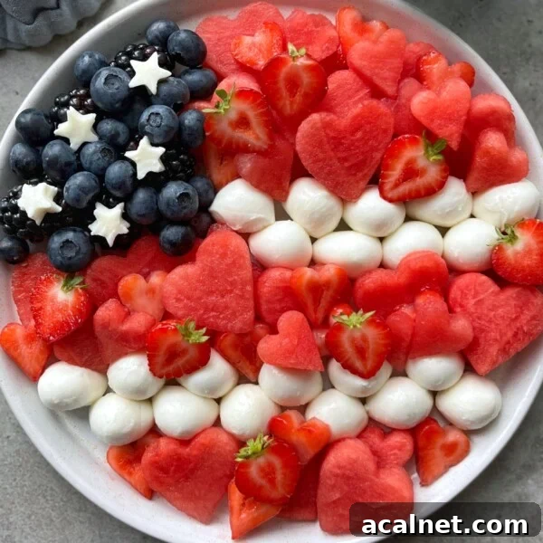 A patriotic plate arranged like the American flag with blueberries, blackberries, mozzarella balls, star-shaped cheese, sliced strawberries, and heart-shaped watermelon bites—perfect for festive food recipes or healthy party dishes.