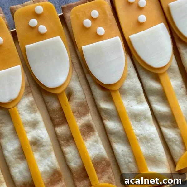 Rectangular crackers topped with cheese and white cheese slices arranged like champagne glasses, with small cheese circles as bubbles—these fun bites are perfect for party food recipes or festive dishes.