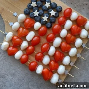Skewers with cherry tomatoes, mozzarella balls, blueberries, and small cheese stars are arranged on a wooden board to resemble the American flag—perfect for healthy bites at festive gatherings or as fun additions to your food recipes.