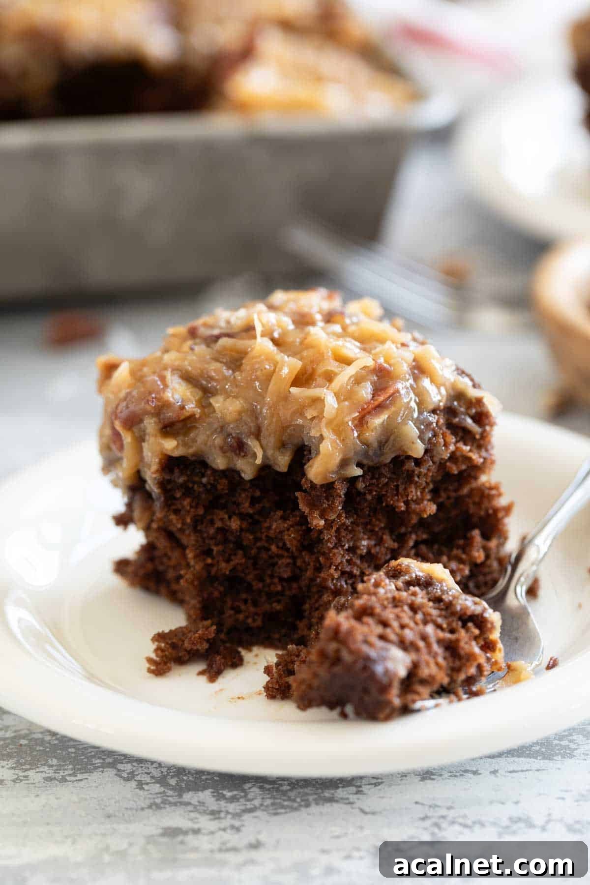 Slice of German Chocolate Cake on a plate with a fork full of cake on the side.