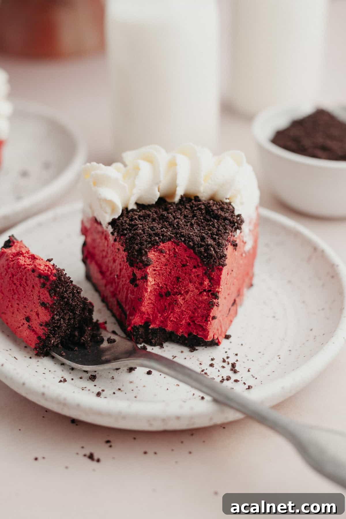 A slice of Oreo red velvet cheesecake on a small plate with a bite taken out of it.