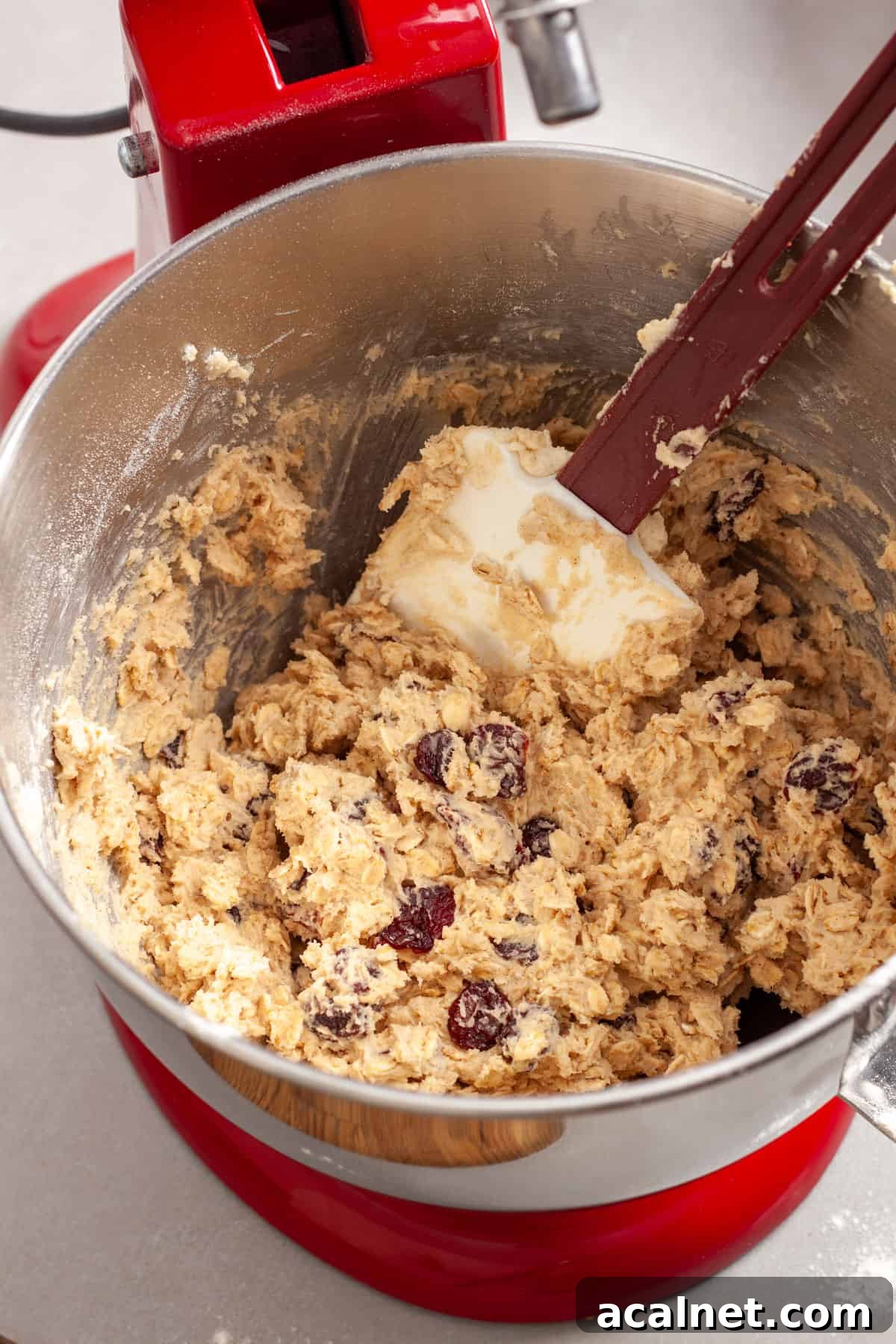 Oatmeal cherry cookie batter getting stirred together by a spatula in a stand mixer.