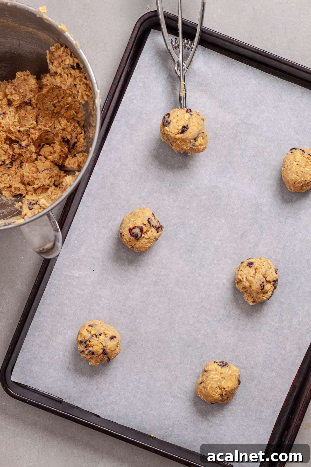 Cherry oatmeal cookie batter portioned out on a parchment-lined baking sheet.