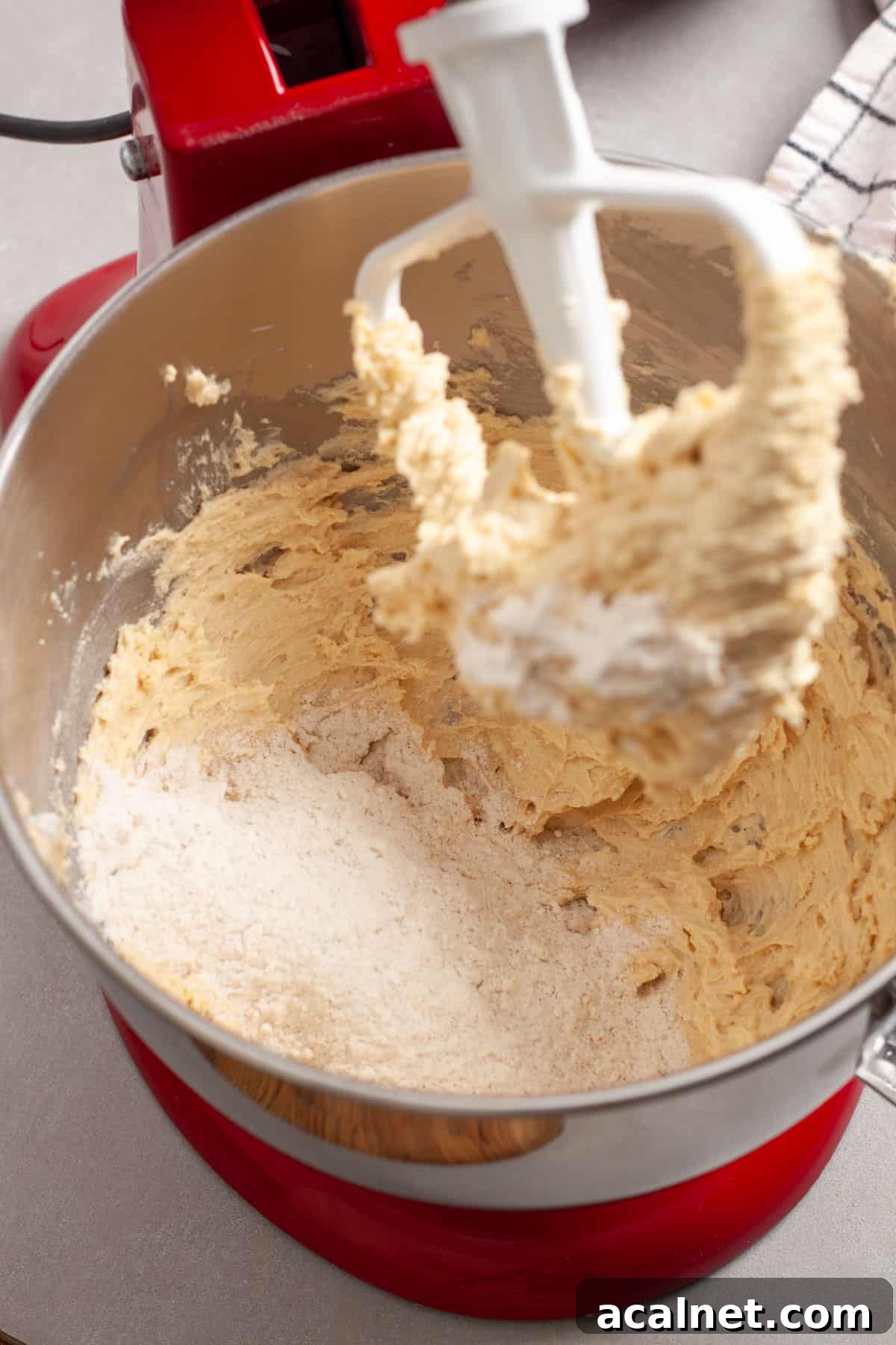 Dry ingredients getting added to a stand mixer with wet ingredients for oatmeal cherry cookies.