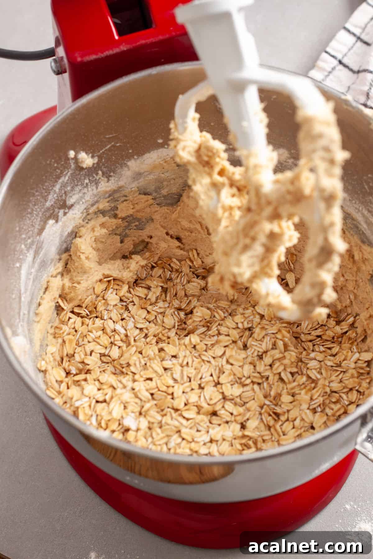 Oats getting added to a stand mixer bowl for cherry oatmeal cookies.