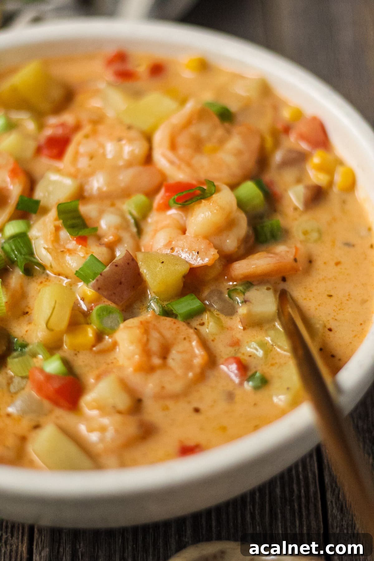 Creamy Cajun Shrimp and Sweet Corn Chowder Recipe 13 side angle shot of creamy cajun shrimp and corn chowder in a white bowl on a wooden surface. Bowl of salt and chopped green onions in top left and bottom right of shot.