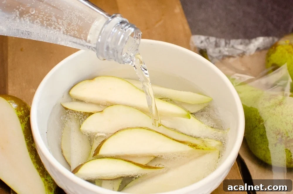 Pouring soda water over fruit, sliced pear and apple in a white bowl