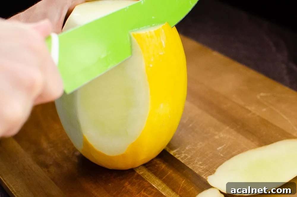 Peeling off the skin of a honeydew melon with a green knife on a wooden chopping board