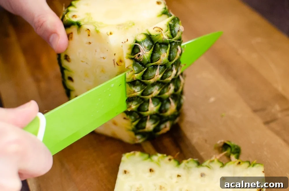 Peeling the skin off a pineapple with a green knife on a wooden chopping board