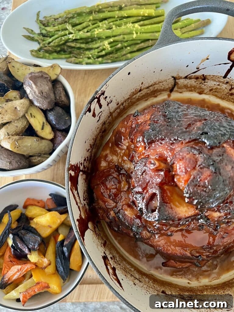 Baked glazed ham in Dutch oven shown with roasted asparagus, roasted rosemary potatoes and roasted rainbow carrots.