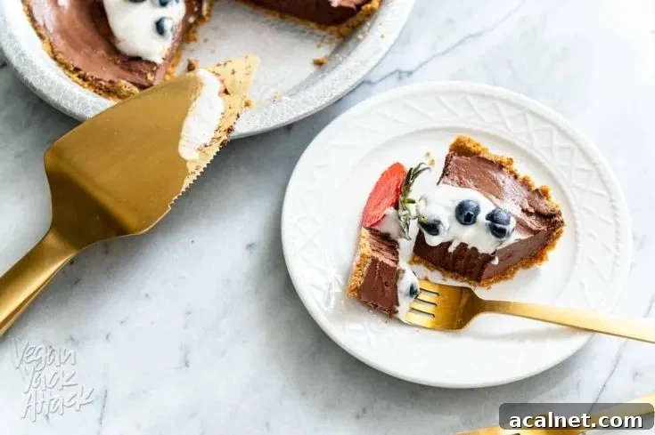Slice of chocolate pie on a plate next to whole pie and gold pie server