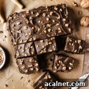 A single layer square chocolate cake on brown parchment paper with nuts sprinkled on top of whipped chocolate ganache frosting.