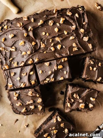 A single layer square chocolate cake on brown parchment paper with nuts sprinkled on top of whipped chocolate ganache frosting.