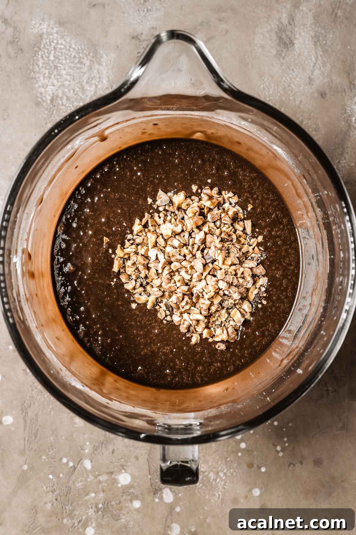 A mixing bowl full of chocolate cake batter with chopped walnuts.