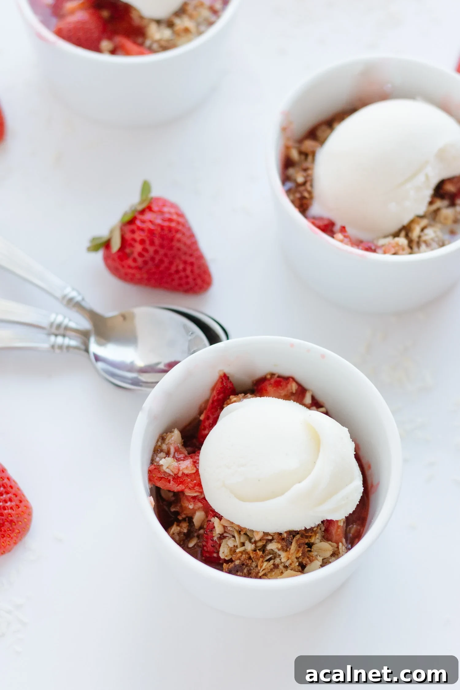 Strawberry Coconut Crisp in three white ramekins topped with a scoop of vanilla ice cream