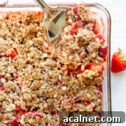 Serving spoon digging into a square glass dish of Strawberry Coconut Crisp.