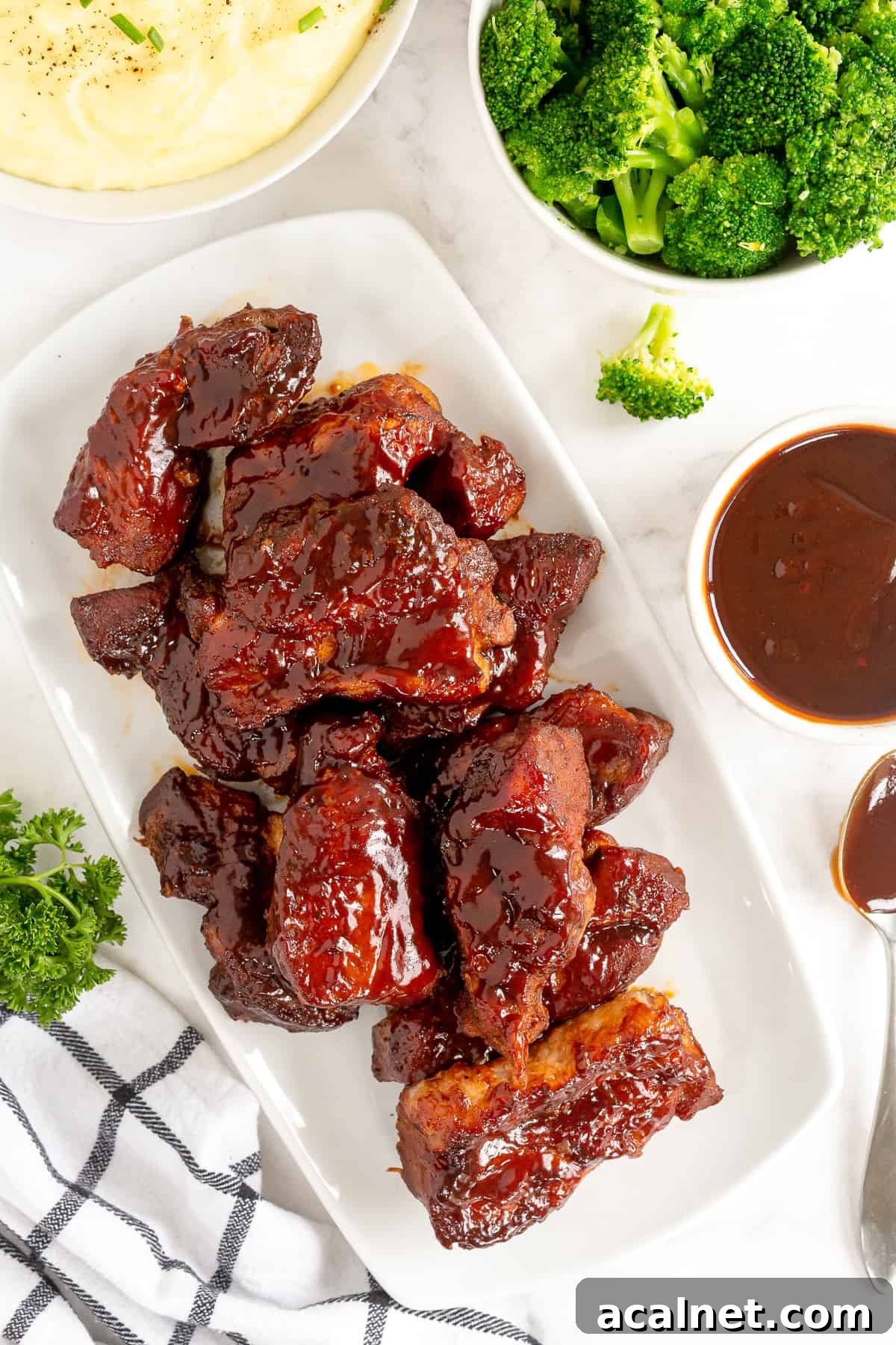A platter of Country Style Ribs with BBQ sauce next to a bowl of mashed potatoes and broccoli.
