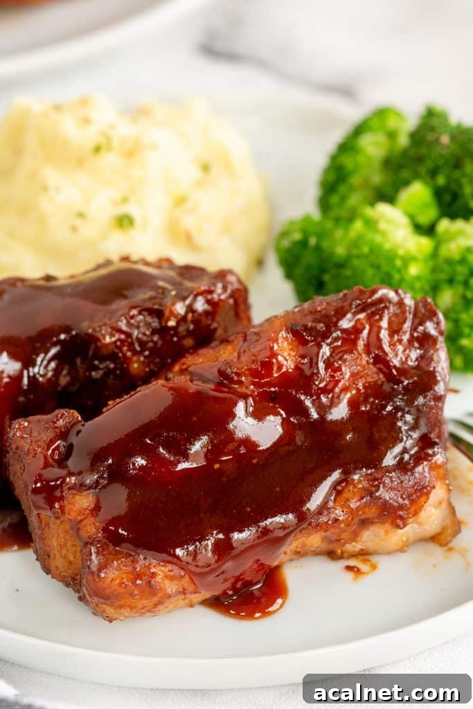 Two country style ribs with bbq sauce on a plate with mashed potatoes and broccoli.