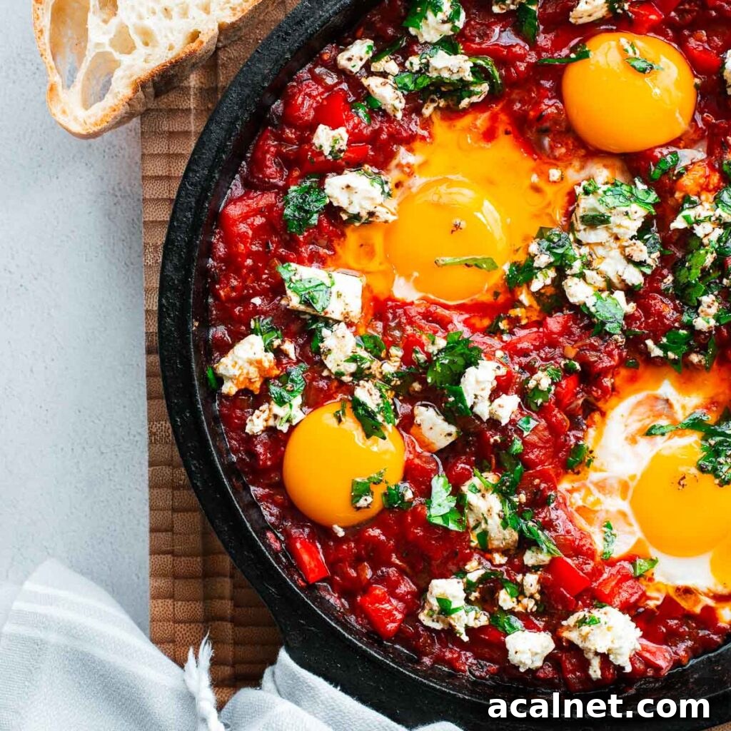 Harissa shakshuka with bright red roasted pepper sauce with soft-cooked eggs and visibly runny yolks topped with feta and parsley in a cast-iron skillet.