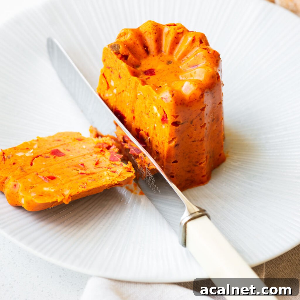 Shaped harissa butter on a small plate sliced with a knife.