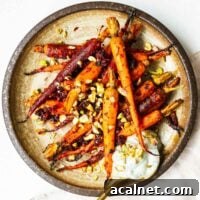 Harissa roasted carrots with chopped pistachios and a dollop of dill yoghurt in a brown ceramic serving plate.