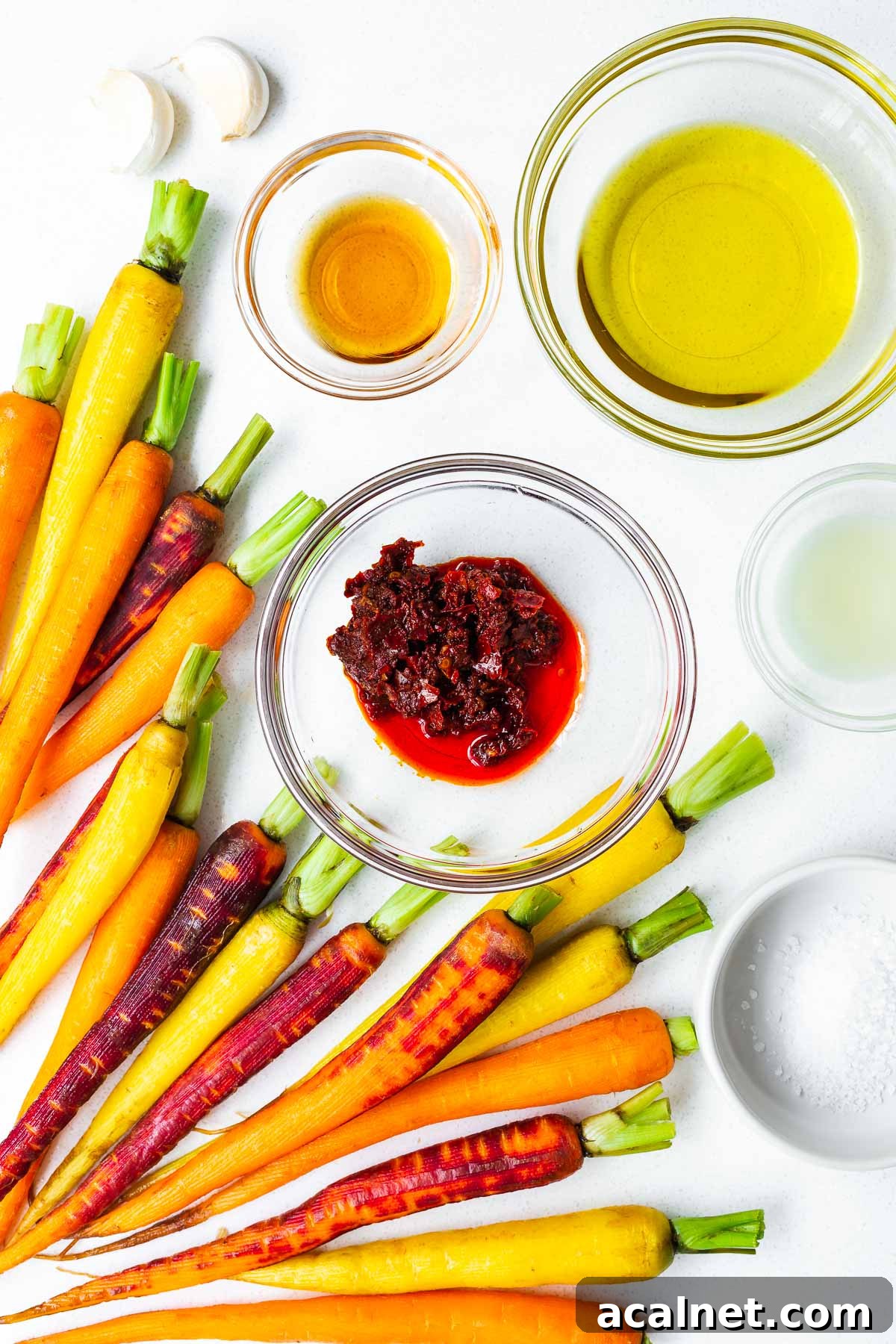 Harissa roasted carrots ingredients arranged in bowls, including harissa paste, garlic, maple syrup, olive oil and lemon juice.