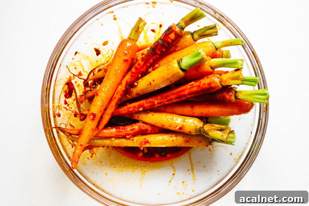 Rainbow carrots tossed in harissa and maple marinade in a glass bowl.