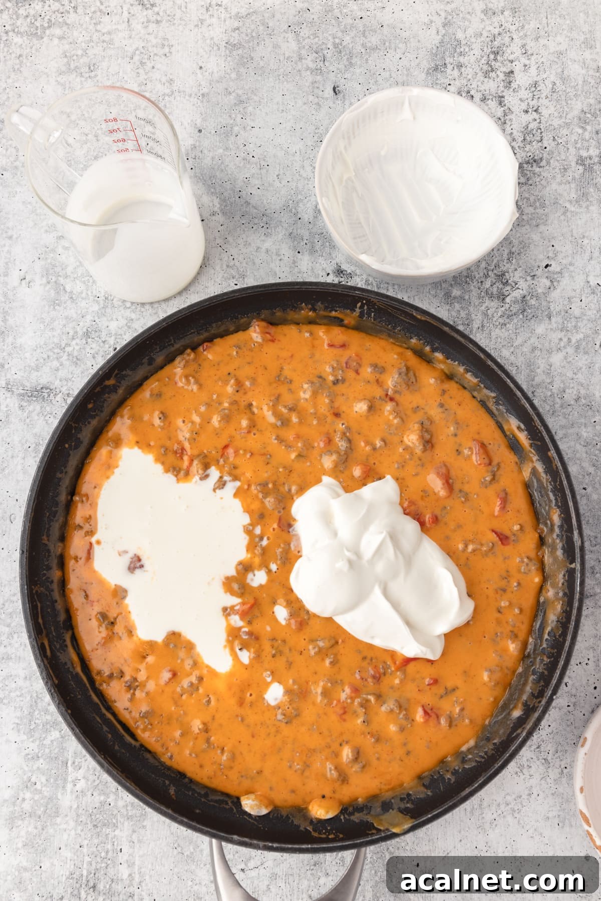 adding in sour cream into the velveeta cheese dip that's melted in a black skillet.