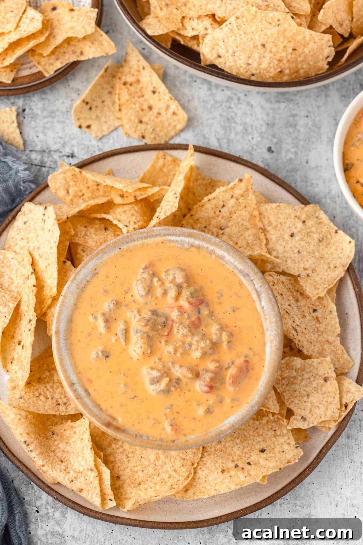 A bowl of creamy cheese dip with sausage and diced tomatoes, accompanied by a plate of tortilla chips.
