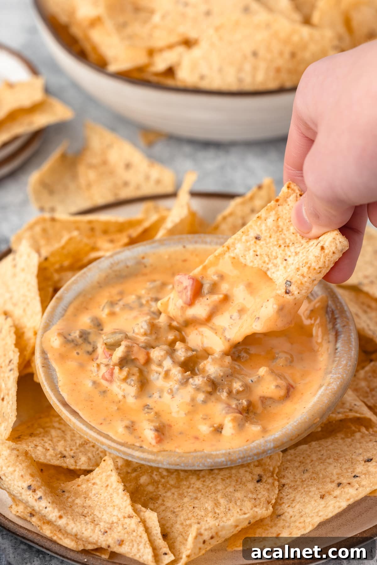 a hand dipping a tortila chip into creamy velveeta sausage dip
