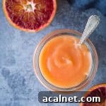 Vegan Blood Orange Curd Recipe — Silky, Zesty Spread 10 close up of a jar of vegan blood orange curd with a spoon in it and sliced blood oranges.