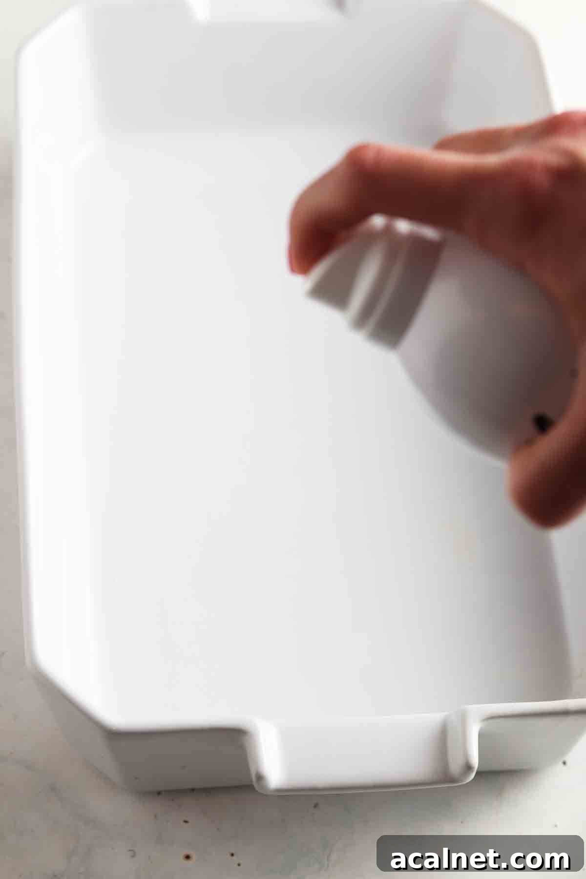Hand holding avocado oil spray over a casserole dish.