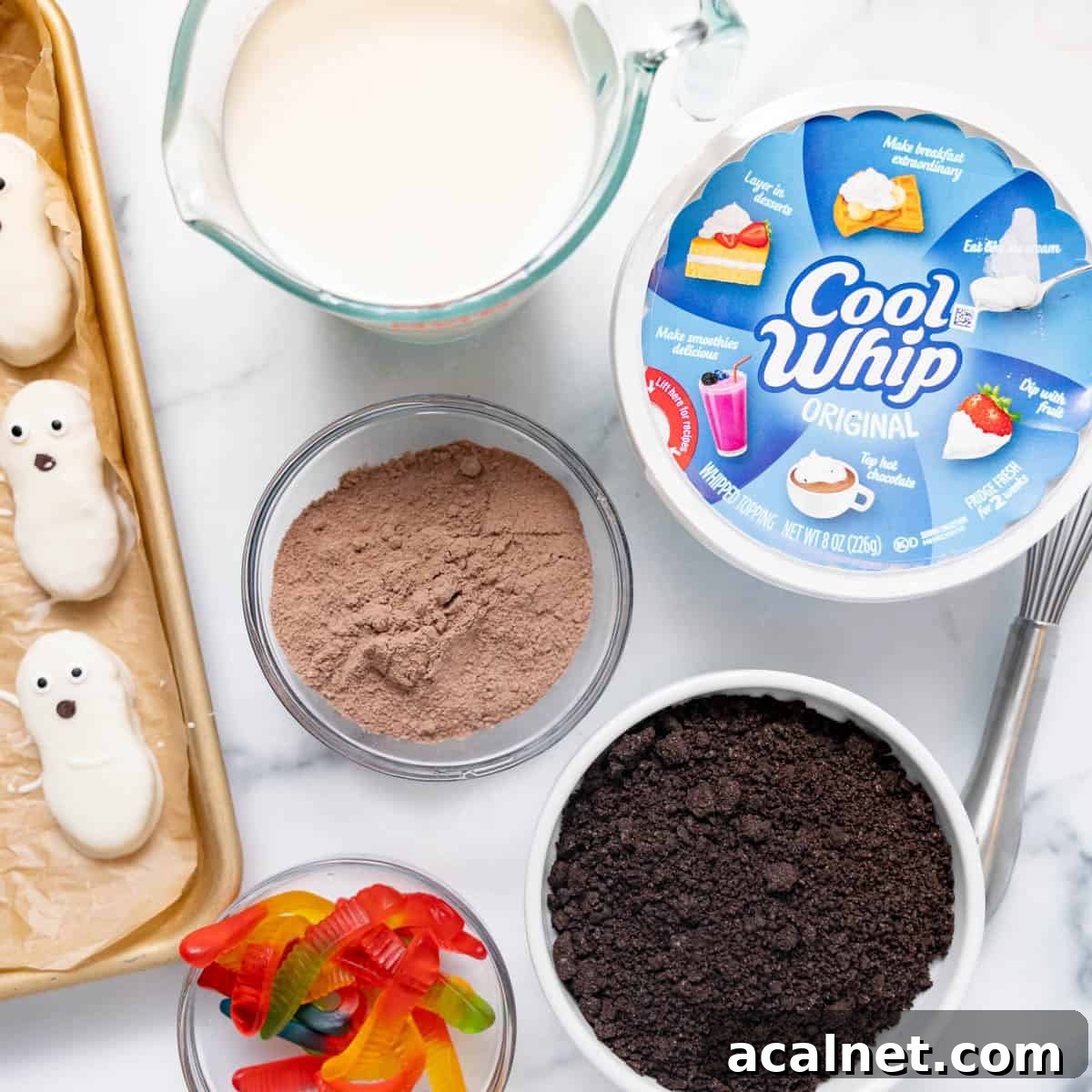 Baking ingredients on a counter, including Cool Whip, chocolate pudding mix, crushed cookies, gummy worms, milk, and tray of ghost-shaped treats.