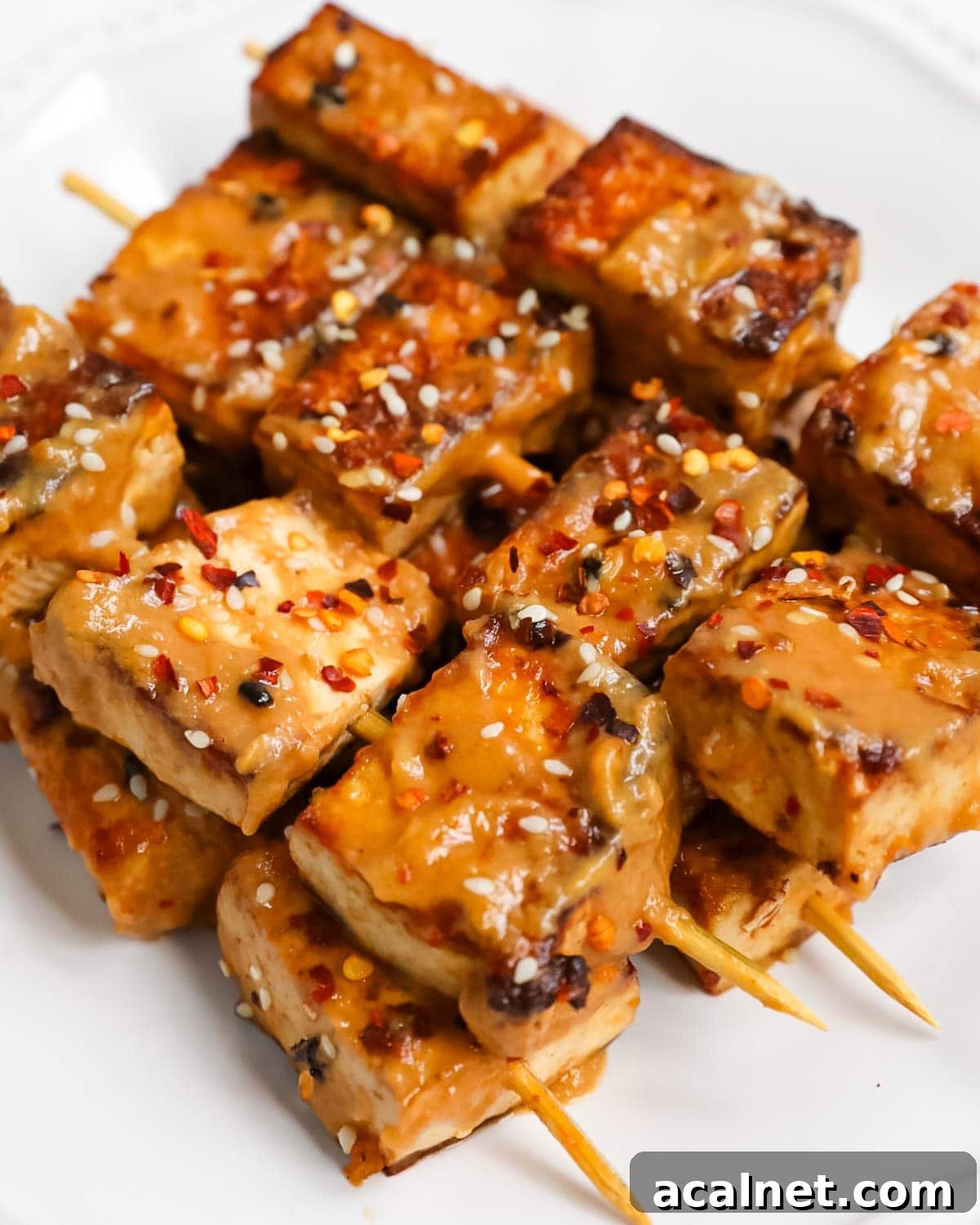 Tofu on skewers with a spicy peanut sauce, sesame seeds, and crushed red pepper flakes on top.