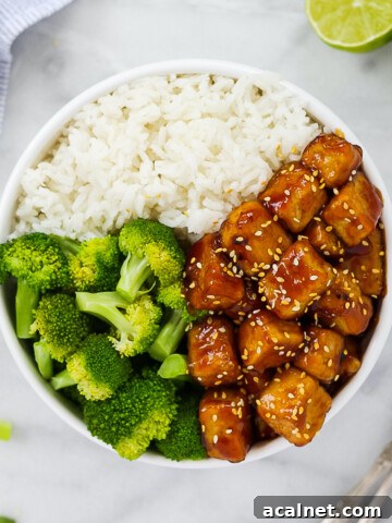 A white bowl holding sesame tofu, white rice, and broccoli.
