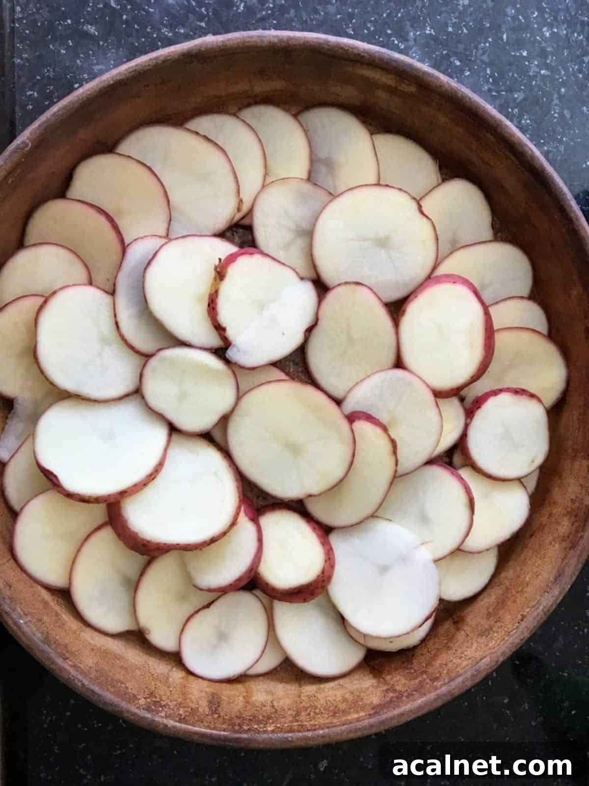 Potato slices layered in a cassreole dish on a table.