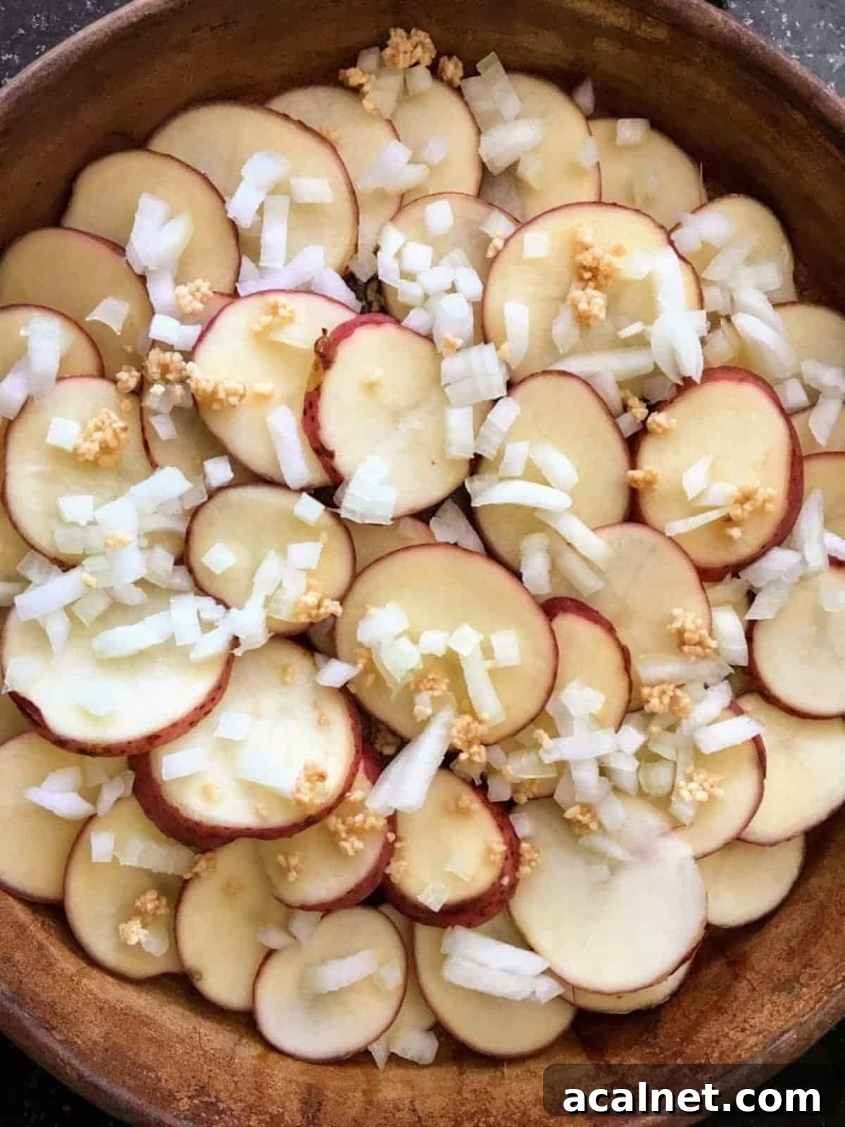 Garlic and diced onion on top of layered potato slices in a casserole dish. 