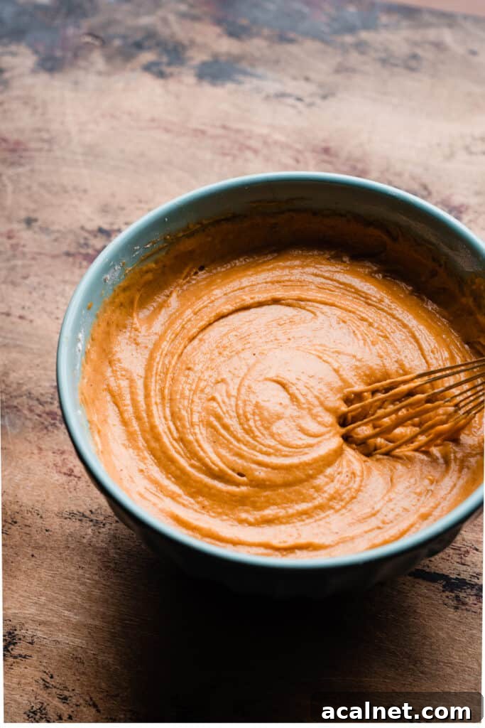 A bowl of bright orange batter being whisked.