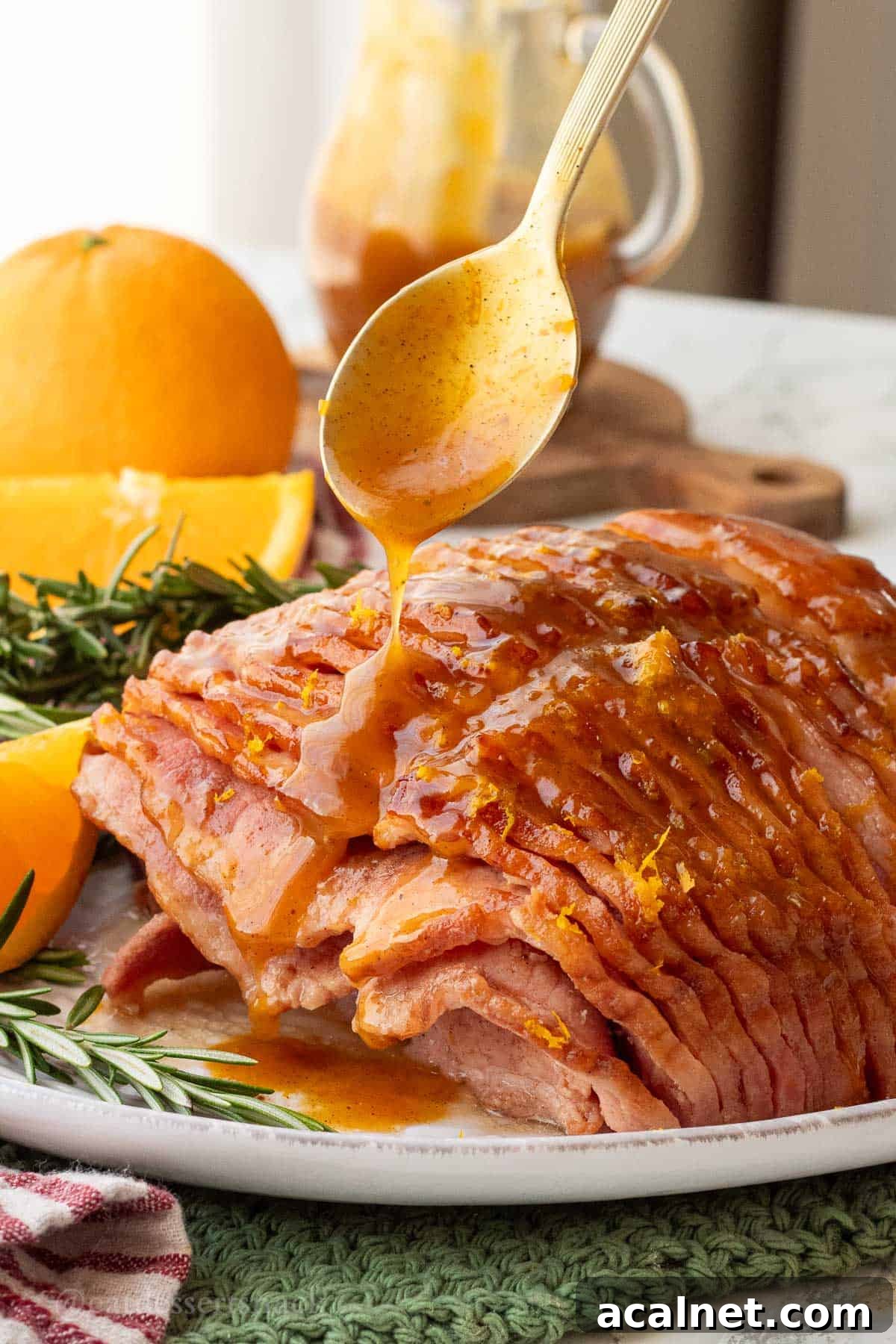 Spoon drizzling orange glaze over cooked ham on platter.