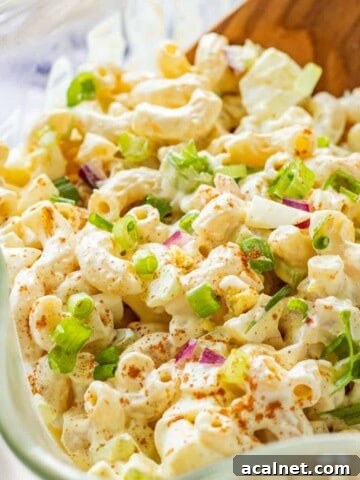 Deviled egg pasta salad in clear glass bowl with wavy edges, paprika and green onions on top.