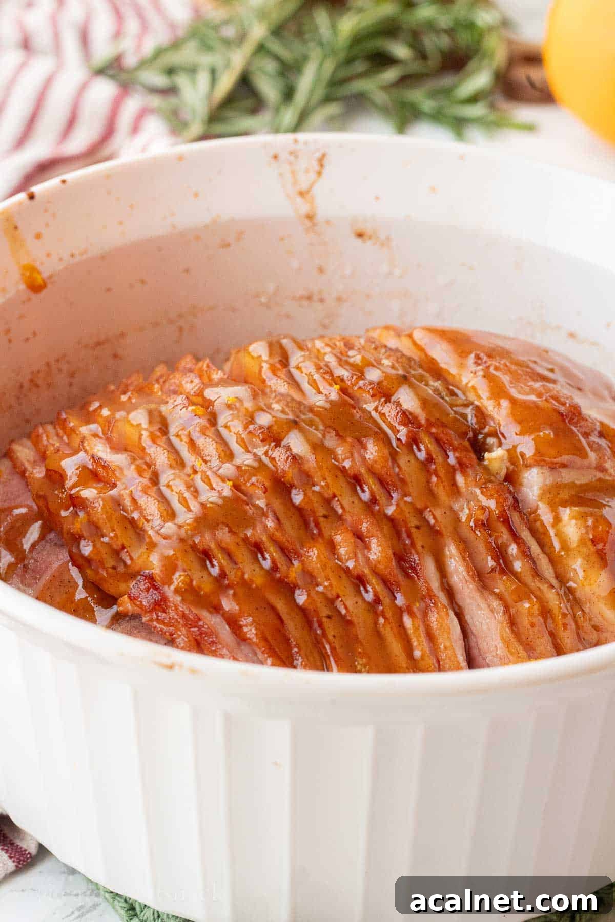 Cooked unglazed ham in white baking dish.