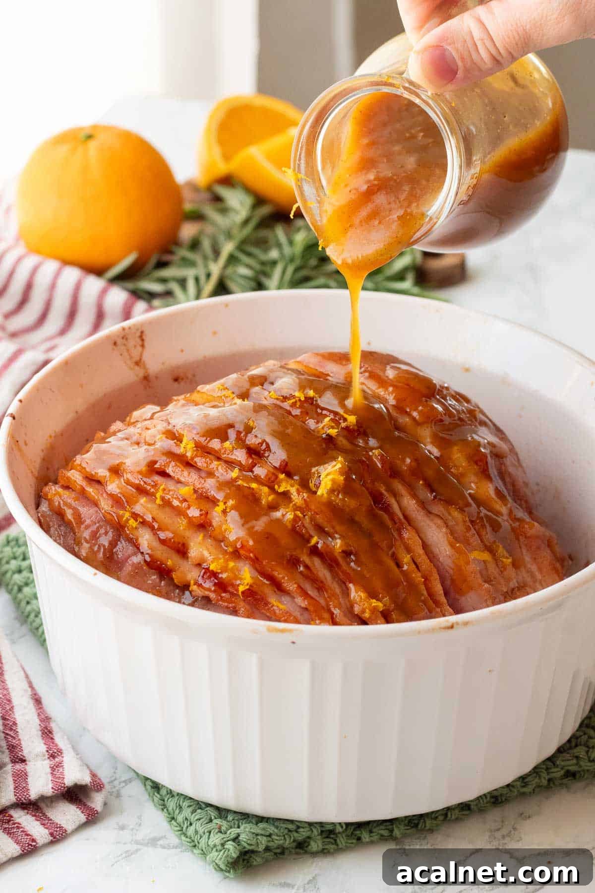 Pouring orange glaze over cooked ham in glass baking dish.