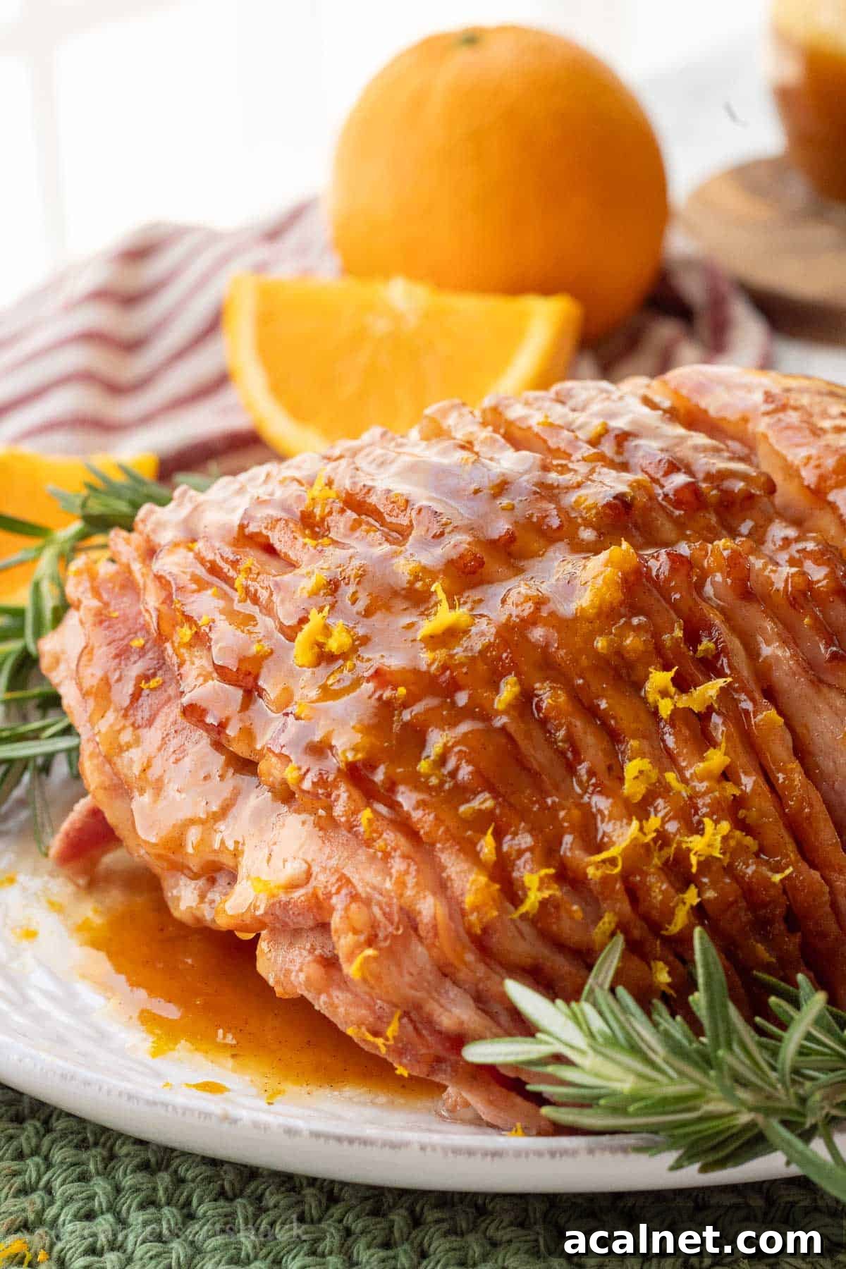 Orange glazed ham on white platter with fresh rosemary.